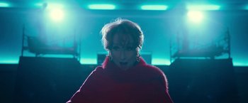 Movie still from “The Prom” (2020), directed by Ryan Murphy – A woman in a red coat is standing in front of a neon light; Medium shot, Low angle