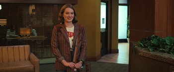 Movie still from “The Prom” (2020), directed by Ryan Murphy – A woman holding a purse and smiling for the camera; Medium shot, Over the shoulder angle