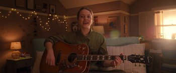 Movie still from “The Prom” (2020), directed by Ryan Murphy – A woman sitting on a couch holding a guitar; Medium shot, Over the shoulder angle