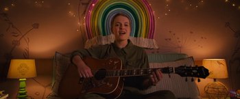 Movie still from “The Prom” (2020), directed by Ryan Murphy – A woman sitting in front of a rainbow holding a guitar; Medium shot, Overhead angle