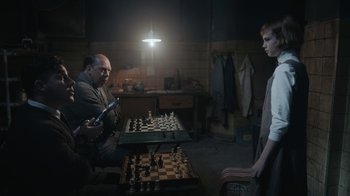 Movie still from “The Queen's Gambit” (2020), directed by Scott Frank – Two men are playing a game of chess in a dark room; Medium shot, Over the shoulder angle