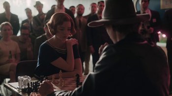 Movie still from “The Queen's Gambit” (2020), directed by Scott Frank – A woman sitting at a chess table in front of a crowd of people; Medium shot, Over the shoulder angle
