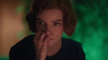 Movie still from “The Queen's Gambit” (2020), directed by Scott Frank – A young woman is sitting in front of a green background; Close Up shot, Low angle