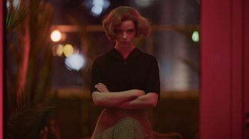 Movie still from “The Queen's Gambit” (2020), directed by Scott Frank – A woman with her arms crossed standing in front of a window; Medium shot, Low angle