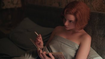 Movie still from “The Queen's Gambit” (2020), directed by Scott Frank – A woman sitting on a couch reading a book; Medium shot, High angle