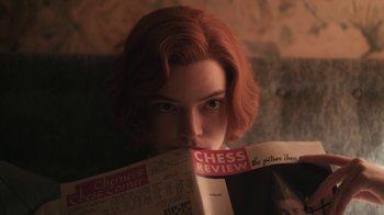 Movie still from “The Queen's Gambit” (2020), directed by Scott Frank – A woman with red hair is reading a magazine; Close Up shot, Over the shoulder angle