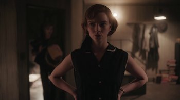Movie still from “The Queen's Gambit” (2020), directed by Scott Frank – A woman standing with her hands on her hips in a dark room; Medium shot, Low angle