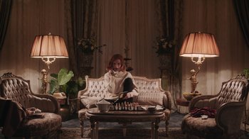 Movie still from “The Queen's Gambit” (2020), directed by Scott Frank – A woman sitting on top of a couch in a living room; Wide shot, High angle