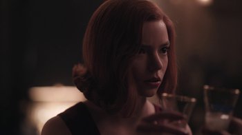 Movie still from “The Queen's Gambit” (2020), directed by Scott Frank – A beautiful woman with red hair holding a glass of wine; Close Up shot, Over the shoulder angle