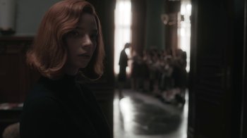 Movie still from “The Queen's Gambit” (2020), directed by Scott Frank – A woman with red hair standing in front of a group of people; Medium shot, Over the shoulder angle