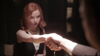 Movie still from “The Queen's Gambit” (2020), directed by Scott Frank – A red haired woman shaking a man's hand in front of a candle holder; Medium shot, Over the shoulder angle