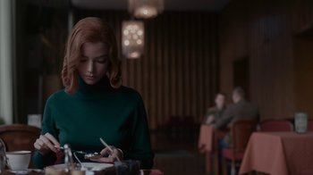 Movie still from “The Queen's Gambit” (2020), directed by Scott Frank – A woman sitting at a table with a plate in front of her; Medium shot, Over the shoulder angle