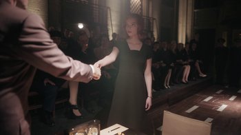 Movie still from “The Queen's Gambit” (2020), directed by Scott Frank – A woman in a black dress shaking hands with a man in a suit; Medium shot, Over the shoulder angle