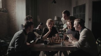 Movie still from “The Queen's Gambit” (2020), directed by Scott Frank – A group of people sitting around a table playing chess; Medium shot, High angle