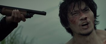Movie still from “The Raid 2” (2014), directed by Gareth Evans – A man with a gun pointed at him with blood on his face; Close Up shot, Low angle
