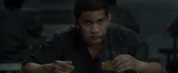 Movie still from “The Raid 2” (2014), directed by Gareth Evans – A man with a knife in his hand and a piece of food in front of him; Close Up shot, Over the shoulder angle