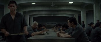Movie still from “The Raid 2” (2014), directed by Gareth Evans – A group of people sitting at a long table eating food; Wide shot, High angle