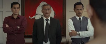 Movie still from “The Raid 2” (2014), directed by Gareth Evans – A man in a suit and tie standing in front of a painting; Medium shot, Low angle