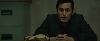 Movie still from “The Raid 2” (2014), directed by Gareth Evans – A man sitting at a table with his hands crossed; Close Up shot, Over the shoulder angle
