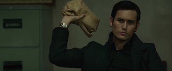 Movie still from “The Raid 2” (2014), directed by Gareth Evans – A man holding a brown bag in one hand and a watch in the other hand; Close Up shot, Low angle