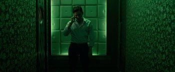 Movie still from “The Raid 2” (2014), directed by Gareth Evans – A man standing in front of a green wall talking on a cell phone; Medium shot, High angle