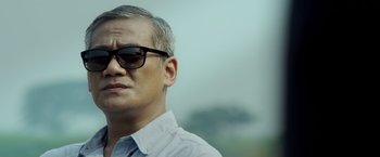 Movie still from “The Raid 2” (2014), directed by Gareth Evans – An older man wearing glasses and a white shirt; Close Up shot, Low angle
