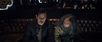 Movie still from “The Raid 2” (2014), directed by Gareth Evans – Two men sitting next to each other on a couch; Medium shot, Over the shoulder angle