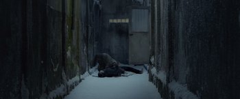 Movie still from “The Raid 2” (2014), directed by Gareth Evans – A person is lying on the ground in the middle of a snowy alley; Wide shot, Overhead angle