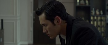 Movie still from “The Raid 2” (2014), directed by Gareth Evans – A man with a black suit and a black shirt is looking to his left; Close Up shot, Over the shoulder angle