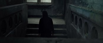 Movie still from “The Raid 2” (2014), directed by Gareth Evans – A person wearing a black hoodie sitting on a set of stairs; Wide shot, Low angle