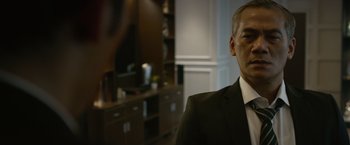Movie still from “The Raid 2” (2014), directed by Gareth Evans – A person wearing a suit in a room; Close Up shot, Over the shoulder angle
