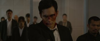 Movie still from “The Raid 2” (2014), directed by Gareth Evans – A man in a black suit with blood on his face; Close Up shot, Over the shoulder angle