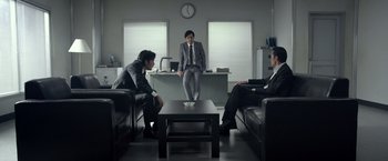 Movie still from “The Raid 2” (2014), directed by Gareth Evans – A group of men sitting around a living room together; Wide shot, Low angle