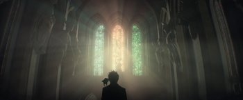 Movie still from “The Sandman” (2022), created by Neil Gaiman – A man holding a cat in front of a stained glass window; Wide shot, Low angle