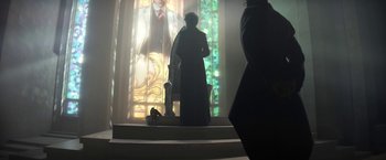 Movie still from “The Sandman” (2022), created by Neil Gaiman – A woman sitting on top of a chair in front of a stained glass window; Wide shot, Over the shoulder angle