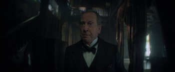 Movie still from “The Sandman” (2022), created by Neil Gaiman – An older man wearing a suit and bow tie; Close Up shot, Low angle