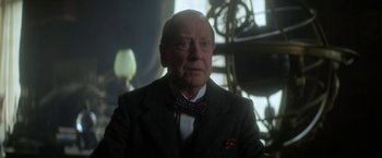 Movie still from “The Sandman” (2022), created by Neil Gaiman – An older man wearing a suit and a bow tie; Close Up shot, Low angle