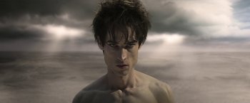 Movie still from “The Sandman” (2022), created by Neil Gaiman – A shirtless man with dark hair is looking at the camera; Close Up shot, High angle