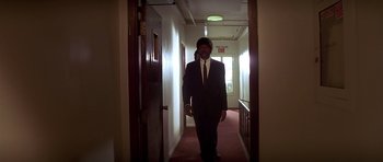 Movie still from “Pulp Fiction” (1994), directed by Quentin Tarantino – A man wearing a suit and tie walking down a hallway; Wide shot, Low angle