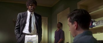 Movie still from “Pulp Fiction” (1994), directed by Quentin Tarantino – A man in a suit standing next to two other men; Medium shot, Over the shoulder angle