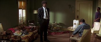 Movie still from “Pulp Fiction” (1994), directed by Quentin Tarantino – A man in a suit standing in a living room; Wide shot, Over the shoulder angle