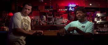 Movie still from “Pulp Fiction” (1994), directed by Quentin Tarantino – A man sitting at a bar with another man standing at the bar; Medium shot, Low angle