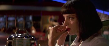 Movie still from “Pulp Fiction” (1994), directed by Quentin Tarantino – A woman sitting at a table with a cigarette in her mouth; Close Up shot, Over the shoulder angle