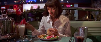 Movie still from “Pulp Fiction” (1994), directed by Quentin Tarantino – A woman sitting in front of a plate of food; Medium shot, Low angle