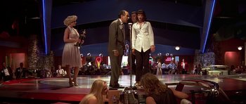 Movie still from “Pulp Fiction” (1994), directed by Quentin Tarantino – A man and a woman stand on a stage with other people; Wide shot, Low angle