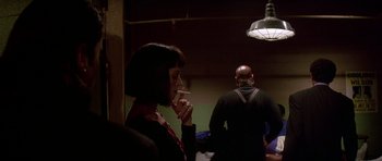 Movie still from “Pulp Fiction” (1994), directed by Quentin Tarantino – A woman smoking a cigarette in front of another man; Medium shot, Over the shoulder angle