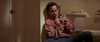 Movie still from “Pulp Fiction” (1994), directed by Quentin Tarantino – A person holding a gun while sitting on the ground; Medium shot, High angle