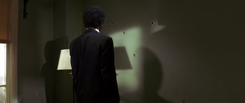 Movie still from “Pulp Fiction” (1994), directed by Quentin Tarantino – A man standing in front of a wall with bullet holes in it; Medium shot, Over the shoulder angle