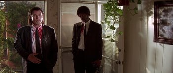 Movie still from “Pulp Fiction” (1994), directed by Quentin Tarantino – A man in a suit standing in front of a door; Medium shot, Low angle