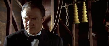 Movie still from “Pulp Fiction” (1994), directed by Quentin Tarantino – A man in a suit and bow tie standing in front of a wall; Close Up shot, Low angle